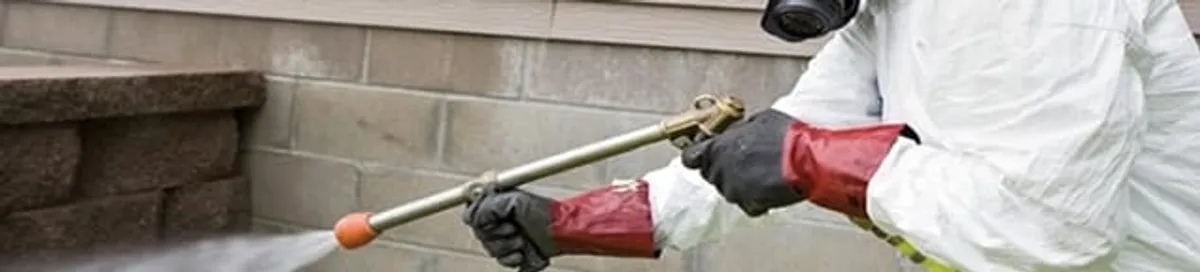 Pest control technician applying exterior insect treatment along a home foundation in Richmond, VA