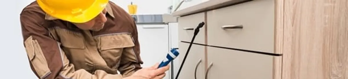 Roach exterminator applying treatment under kitchen cabinets in Richmond, VA