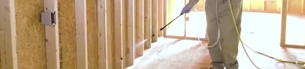 Termite treatment technician applying spray along framing and unfinished walls in Richmond, VA