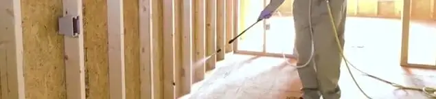 Termite treatment technician applying spray along framing and unfinished walls in Richmond, VA